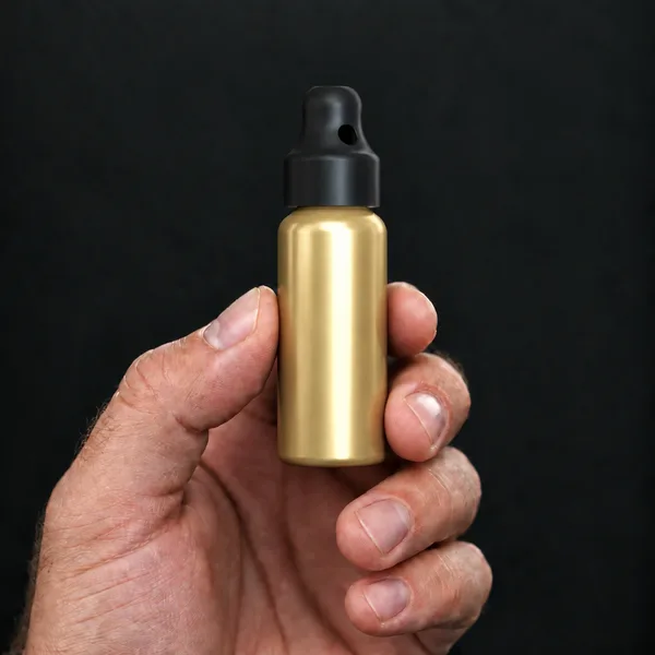 Main tenant un flacon 24 ml en aluminium, doré avec un bouchon sniffer SN*F Small