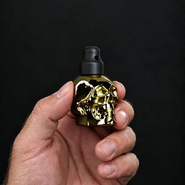 Main tenant un flacon 24 ml tête de mort, doré avec un bouchon sniffer SN*F X-Small